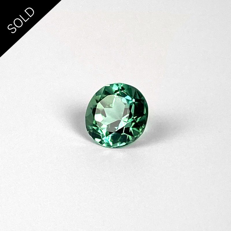 Dieser Edelstein ist ein runder grüner blauer Turmalin im Brillant-Schliff.