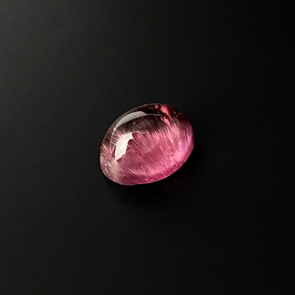 Der rosafarbene ovale Turmalin in cabochon schliff, besitzt kleine einzigartige Einschlüsse, die bei genauer Betrachtung sichtbar sind. Bei Lichtreflexion kommt der Katzenauge-Effekt zum Vorschein.