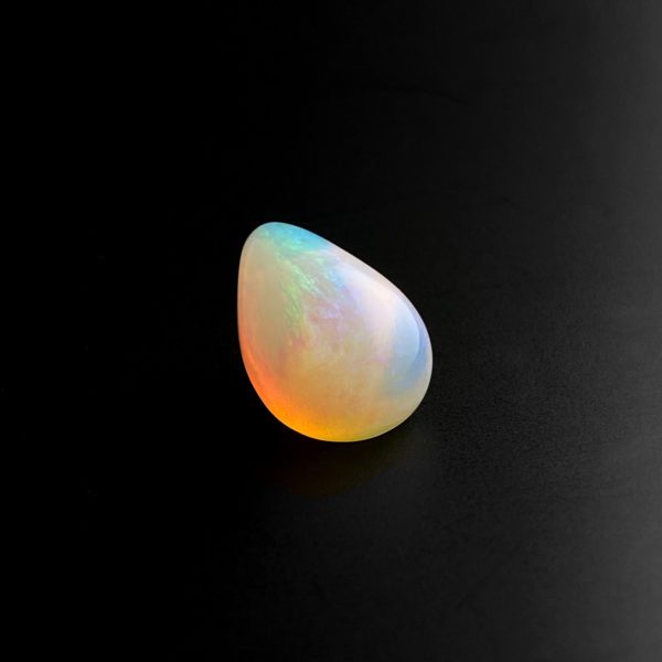 Der in Tropfen Form geschliffene milchige Edel Opal reflektiert je nach Lichteinfall ein schimmerndes buntes Farbenspiel.