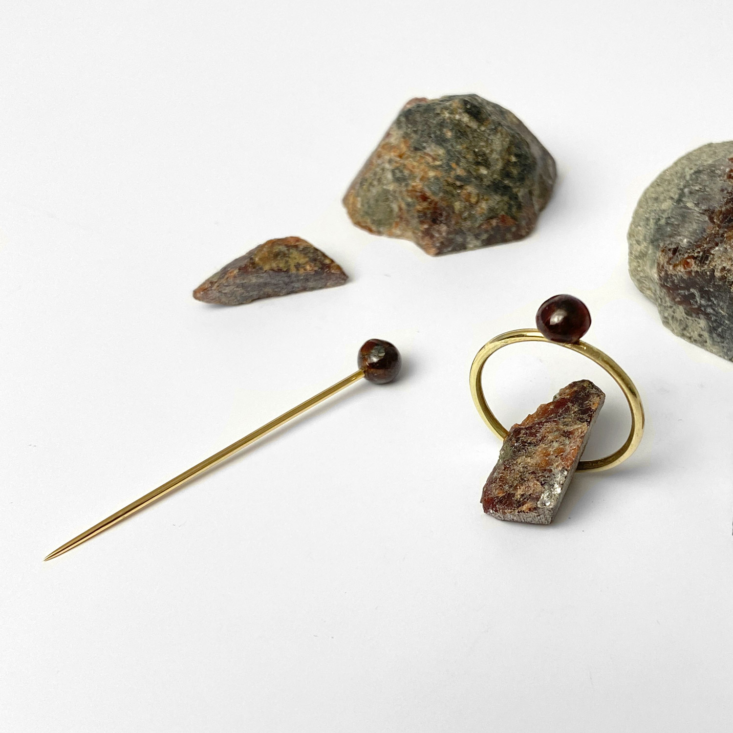 Diese Schmuckstücke sind ein roter Pin und ein Ring mit einem von Hand geschliffenen Granat und Gold.